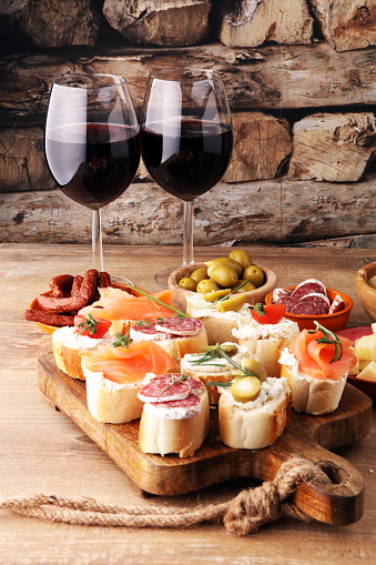 Italian antipasti wine snacks set. Cheese variety, Mediterranean olives, pickles, salami, salmon, tomatoes, artichokes and wine in glasses. Spanish tapas